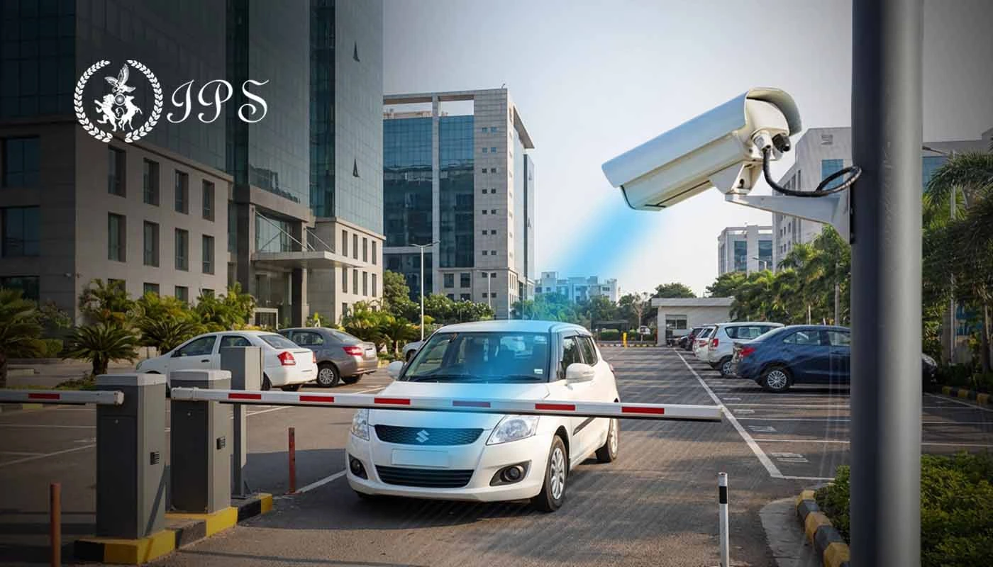 Security camera monitoring a gated parking entrance with a car waiting at the barrier outside a modern office building.